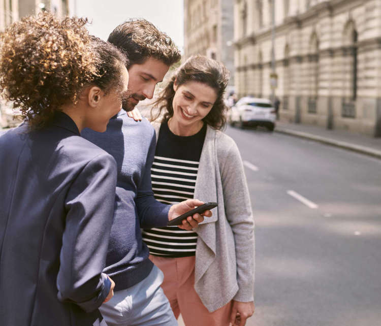 Чоловік і дві жінки дивляться на екран смартфона на вулиці